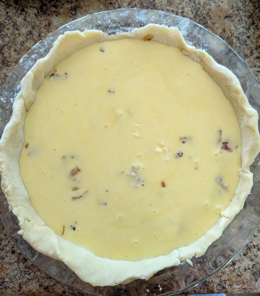 Unbaked quiche Lorraine in pie dish with bacon, cheese, and egg mixture

