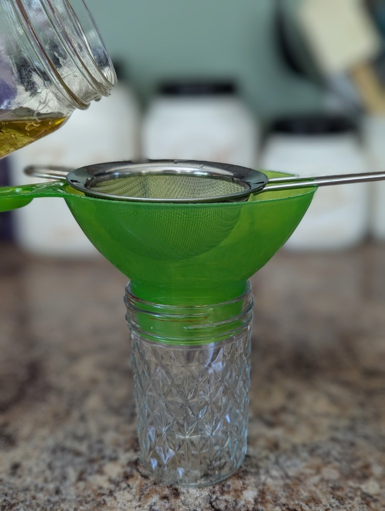 Straining calendula oil through a fine mesh strainer
