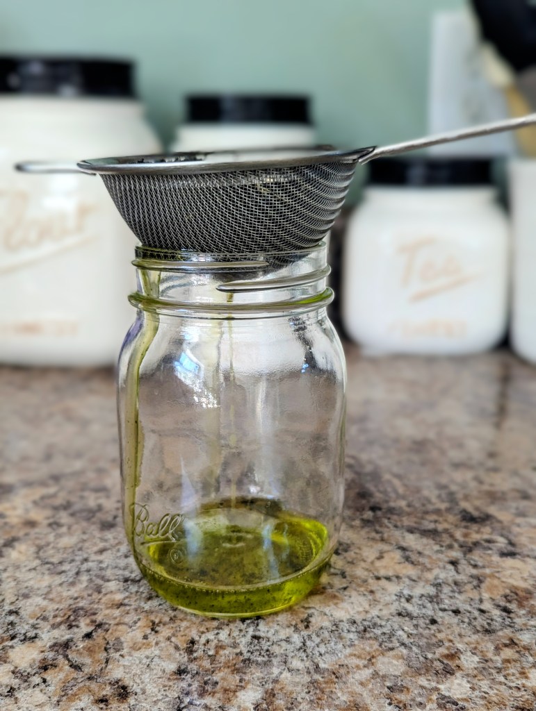 Straining stinging nettle hair oil through fine mesh strainer