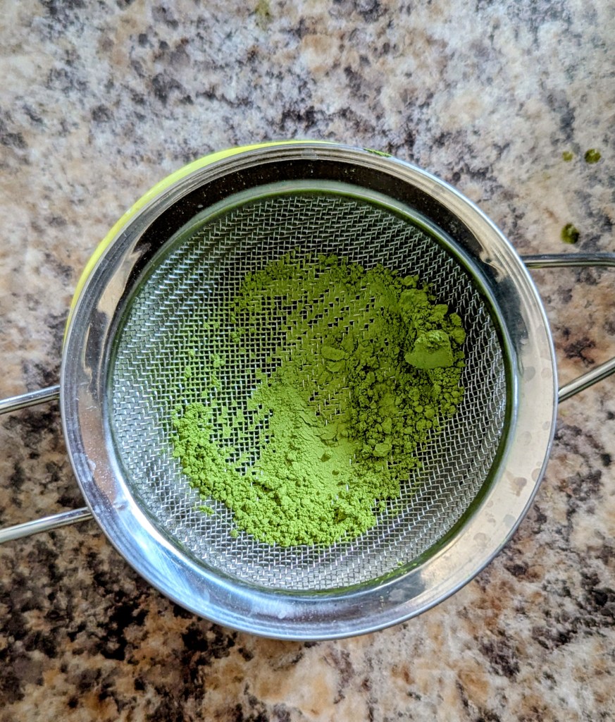 sifting matcha powder for a strawberry matcha