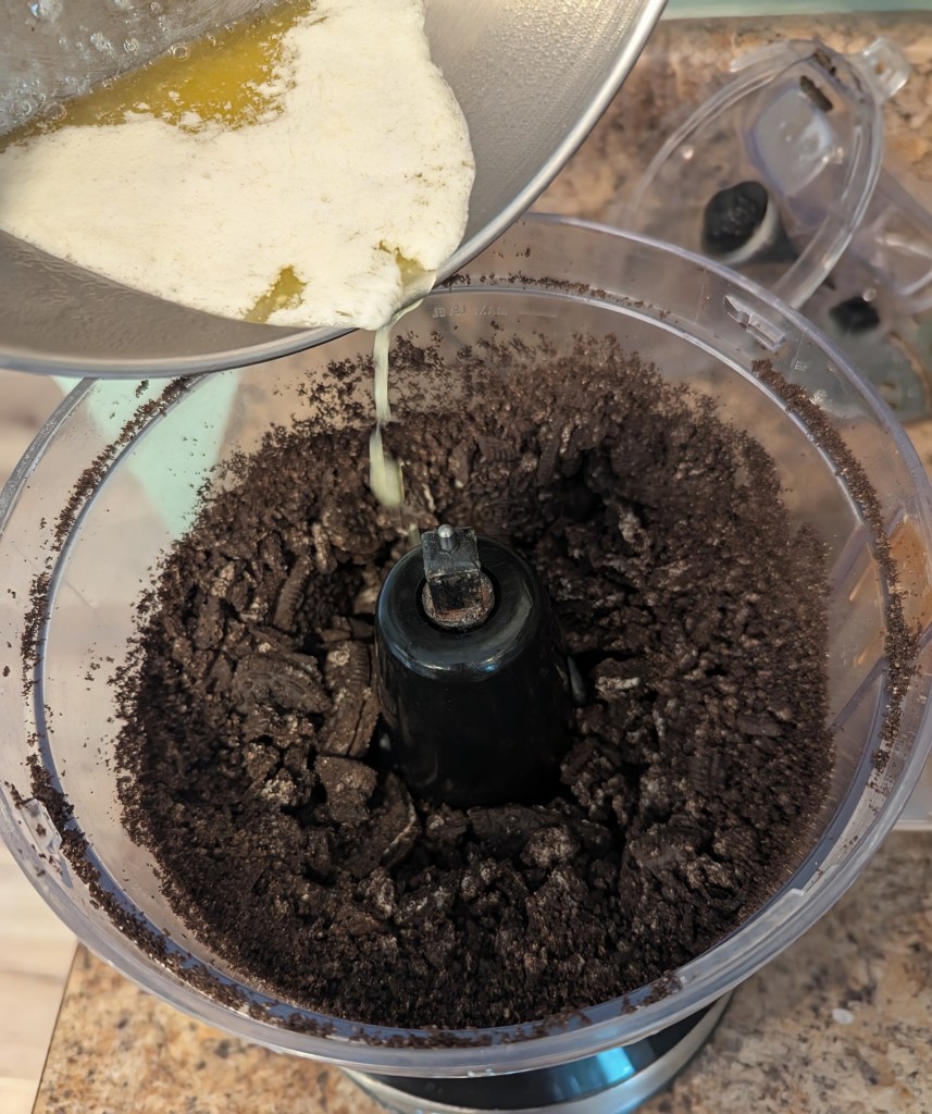Pouring melted butter into a food processor for oreo cookie crust