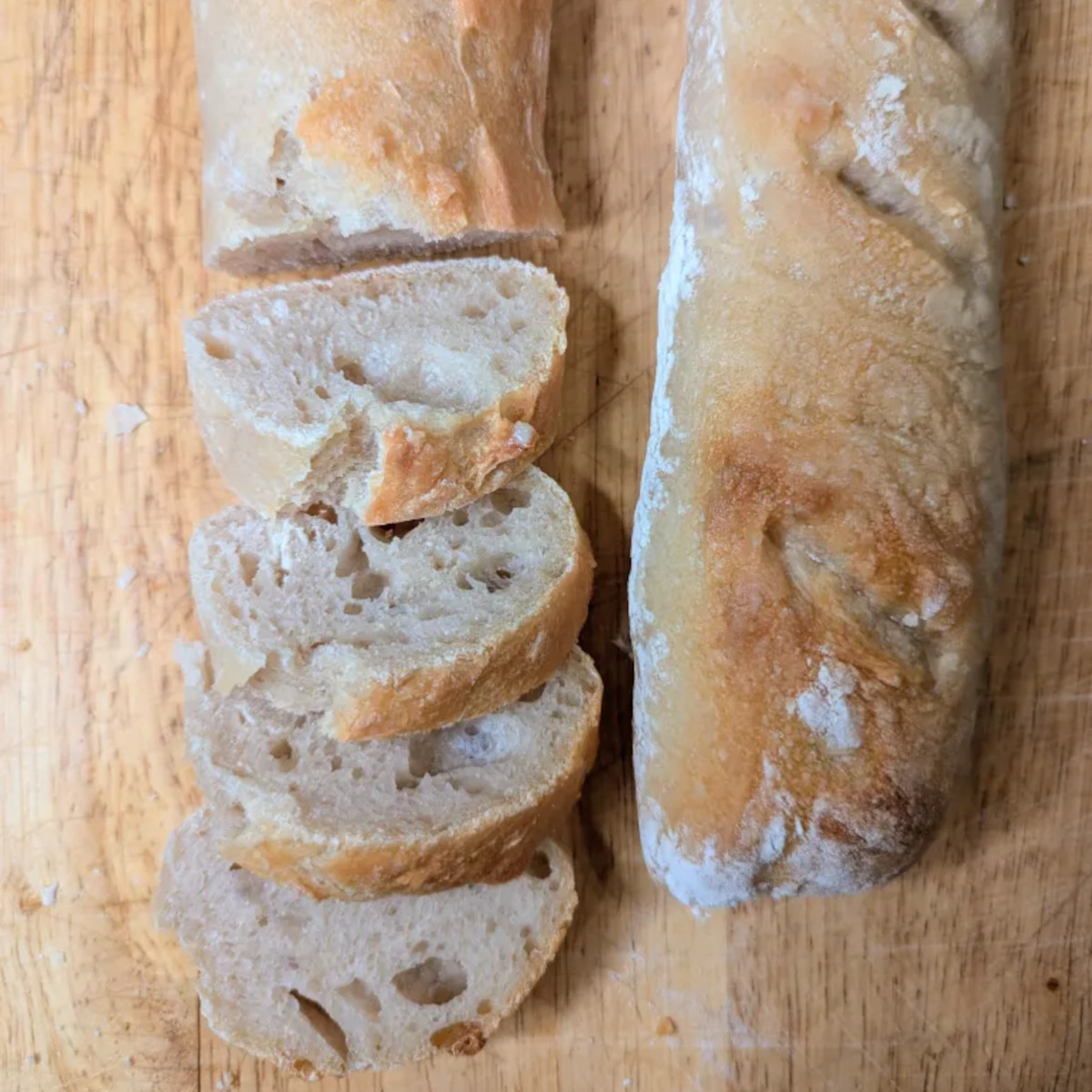 Freshly baked and sliced sourdough baguettes with a crispy scored crust resting on a farmhouse table.