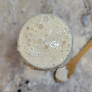Top-down aerial view of a bubbly, active sourdough starter fermenting inside a glass jar
