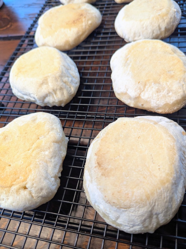 Golden sourdough English muffins on a cooling rack